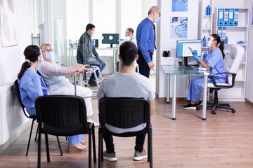 Nurse taking notes on clipboard wearing visor and sterile gloves against coronavirus while questioning elderly man in hospital waiting area. Social distancing, medic, covid-19, man, worried,