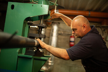 Male engineer metalworker industrial experienced operator technician worker working on machine with...