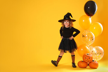 Cute little girl with pumpkins and balloons wearing Halloween costume on yellow background. Space...