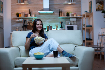 Woman laughing watching tv and eats snacks. Young happy, excited, amused, home alone lady enjoying...