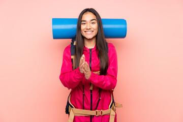 Young mountaineer Indian girl with a big backpack isolated on pink background applauding
