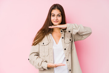 Young caucasian woman posing in a pink background holding something with both hands, product presentation.