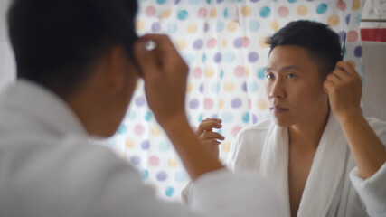 Close up mirror reflection of handsome young asian man combing hair in bathroom