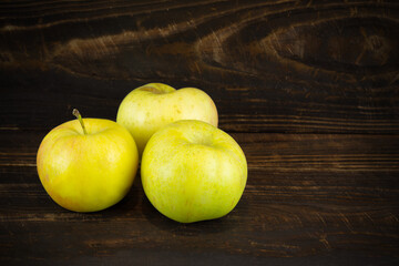 Three yellow apples on brown wooden plank background.