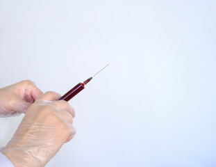 A hand in a latex glove holds a syringe. Doctor holds a syringe for vaccination.