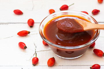 Homemade rosehip marmalade in glass bowl with fresh rose hip fruits on rustic background ( rosa...