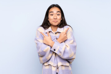 Young Indian woman isolated on blue background pointing to the laterals having doubts