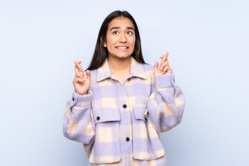 Young Indian woman isolated on blue background with fingers crossing and wishing the best