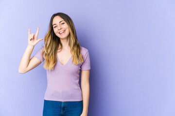 Fototapeta premium Young caucasian woman isolated on purple background showing a horns gesture as a revolution concept.