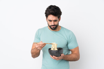 Young handsome man with beard over isolated white background holding a bowl of noodles with chopsticks