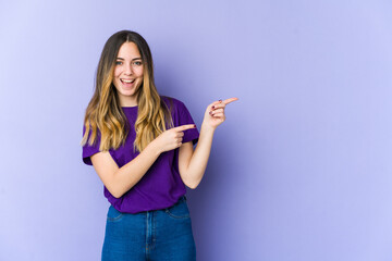 Young caucasian woman isolated on purple background pointing with forefingers to a copy space, expressing excitement and desire.