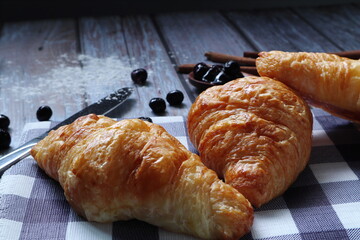 baked butter French croissants are on the wooden table wiht a knife and cinnamon rolls during breakfast in the coffee shop of the resort hotel in summer holiday with happy family