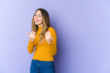 Young caucasian woman isolated on purple background pointing with finger at you as if inviting come closer.