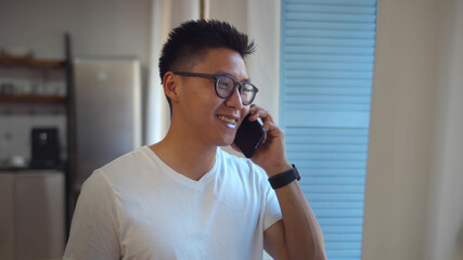 Handsome young asian man having phone call relaxing near window in living room