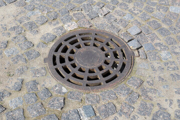 Metal sewer manhole with holes on the cobbled pavement.
