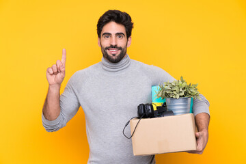 Young handsome man with beard making a move while picking up a box full of things over isolated...