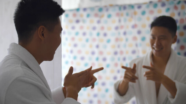 Confident young asian man enjoying his reflection in bathroom mirror