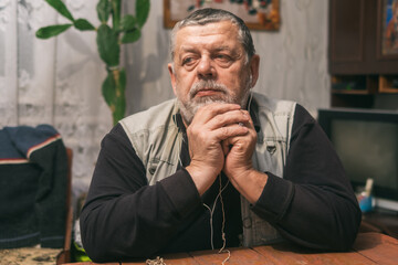 Indoor portrait of sad Ukrainian peasant sitting at wooden table and thinking