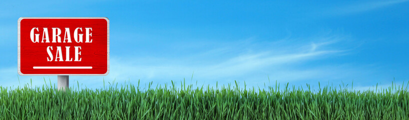 Sign with phrase GARAGE SALE in green grass under blue sky, banner design