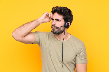 Telemarketer man working with a headset over isolated yellow background having doubts and with confuse face expression