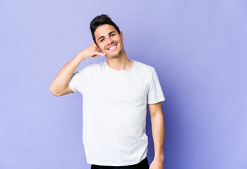 Young caucasian man isolated on purple background showing a mobile phone call gesture with fingers.