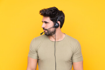 Telemarketer man working with a headset over isolated yellow background looking side