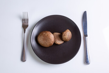 Raw Jersey cow mushrooms in a black plate and a knife and fork nearby on a white background top view. Horizontal orientation. High quality photo