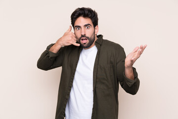 Young handsome man with beard over isolated background making phone gesture and doubting