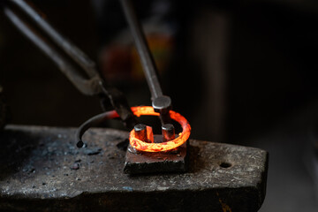 Blacksmith bends iron rod on the anvil with tool