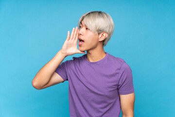 Young asian man over isolated blue background shouting with mouth wide open to the lateral