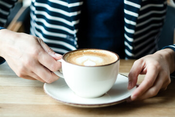 Coffee, cappuccino, latte, cup, work, study, woman, morning. Woman in blue jacket with white lines holding a cup with cappuccino. Close up.