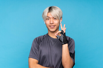 Young asian sport man over isolated blue background showing ok sign with fingers