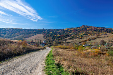 Naklejka premium Dirt road to church in small village among colorful hills in Carpathian Mountains, Ukraine at sunny autumn day