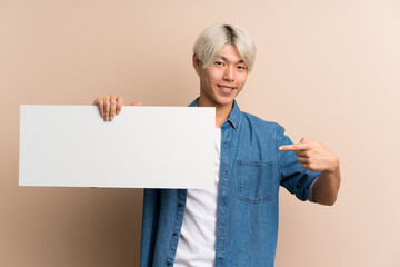 Young asian man over isolated background holding an empty white placard for insert a concept