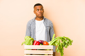 Young farmer man isolated on a beige background confused, feels doubtful and unsure.