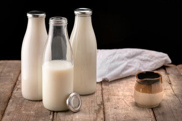 Bottles of fresh milk with small jug on rustic table