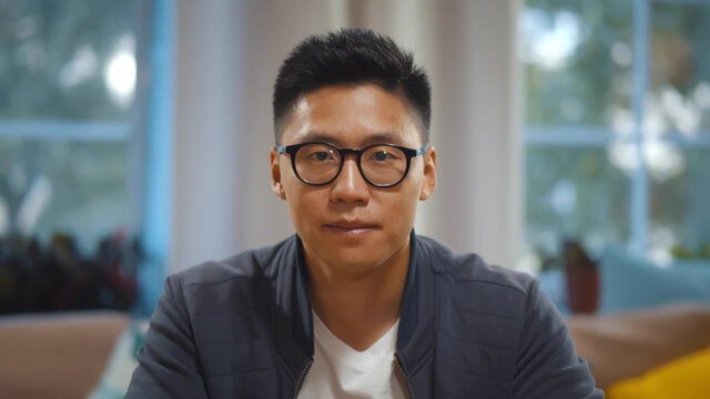 Portrait of asian man in glasses talking online via video call sitting at home