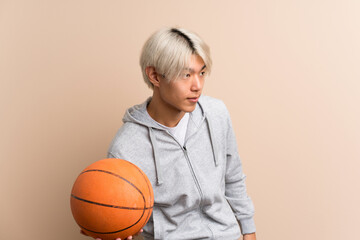 Young asian man over isolated background with ball of basketball