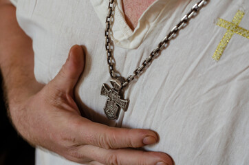An adult man in a linen shirt with a silver cross underwear prays.