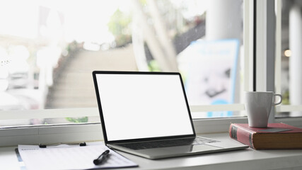 Mock up laptop with white screen on modern workspace with cup, book and document.