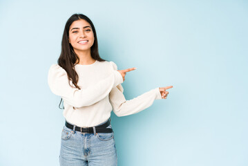Young indian woman isolated on blue background excited pointing with forefingers away.