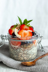 Chia pudding portion with strawberries and toasted coconut, mint, white background
