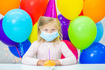 Fototapeta na wymiar Little girl wearing party cap sits at home with birthday cupcake during the coronavirus epidemic