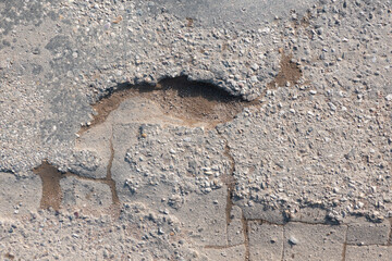 A fragment of the asphalt road surface in poor condition. There is a hole, cracks, traces of repair at different times. Background. Texture.