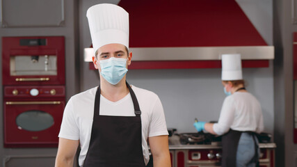 Fototapeta na wymiar Portrait of male chef wearing face protective medical mask at restaurant kitchen