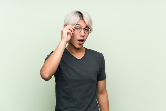 Young asian man over isolated green background with glasses and surprised