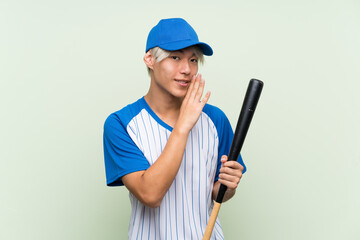 Young asian man playing baseball over isolated green background whispering something