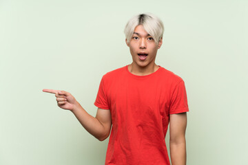 Young asian man over isolated green background surprised and pointing finger to the side