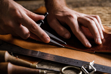 Close up of a shoemaker or artisan worker hands. Leather craft tools on old wood table. Leather craft workshop.