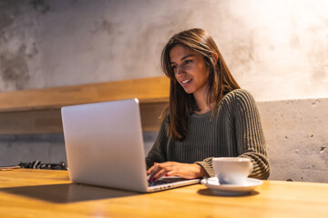 Fototapeta premium A young Caucasian brunette entrepreneur working from a coffee shop. Having a coffee and working with the computer